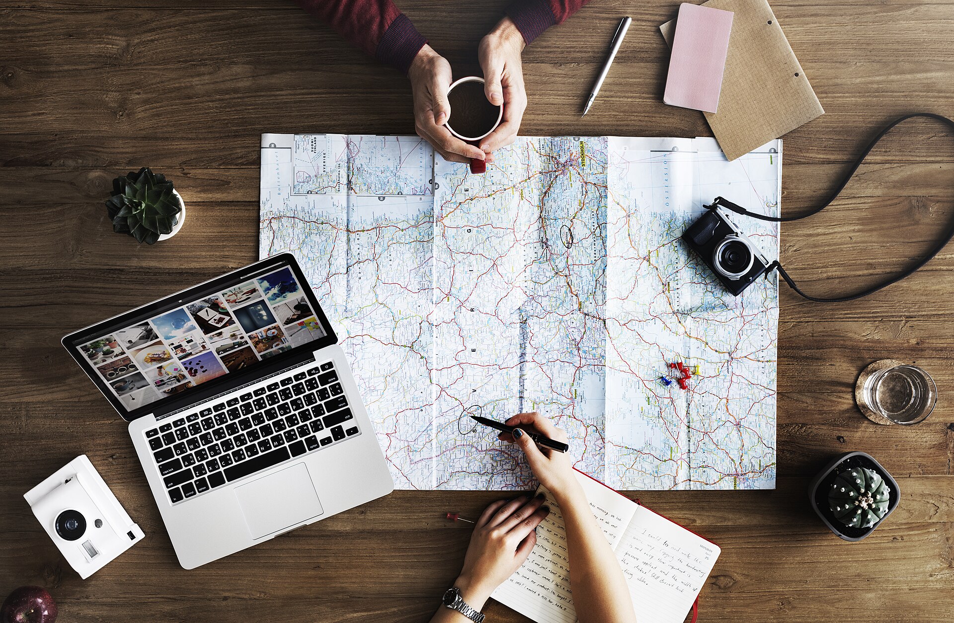 Hands planning a route with a map, laptop and notebooks