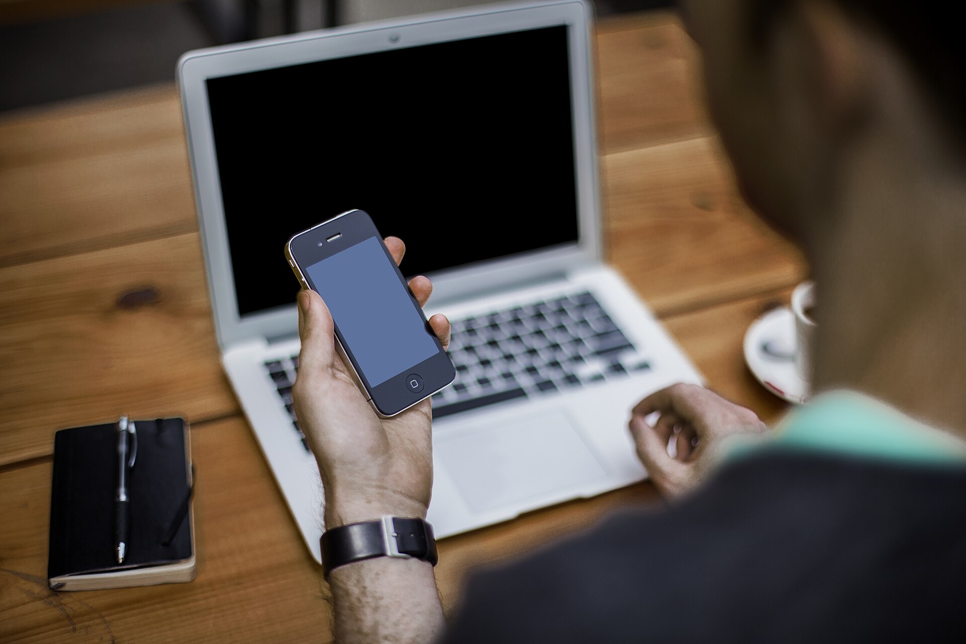 A person using a phone beside a laptop