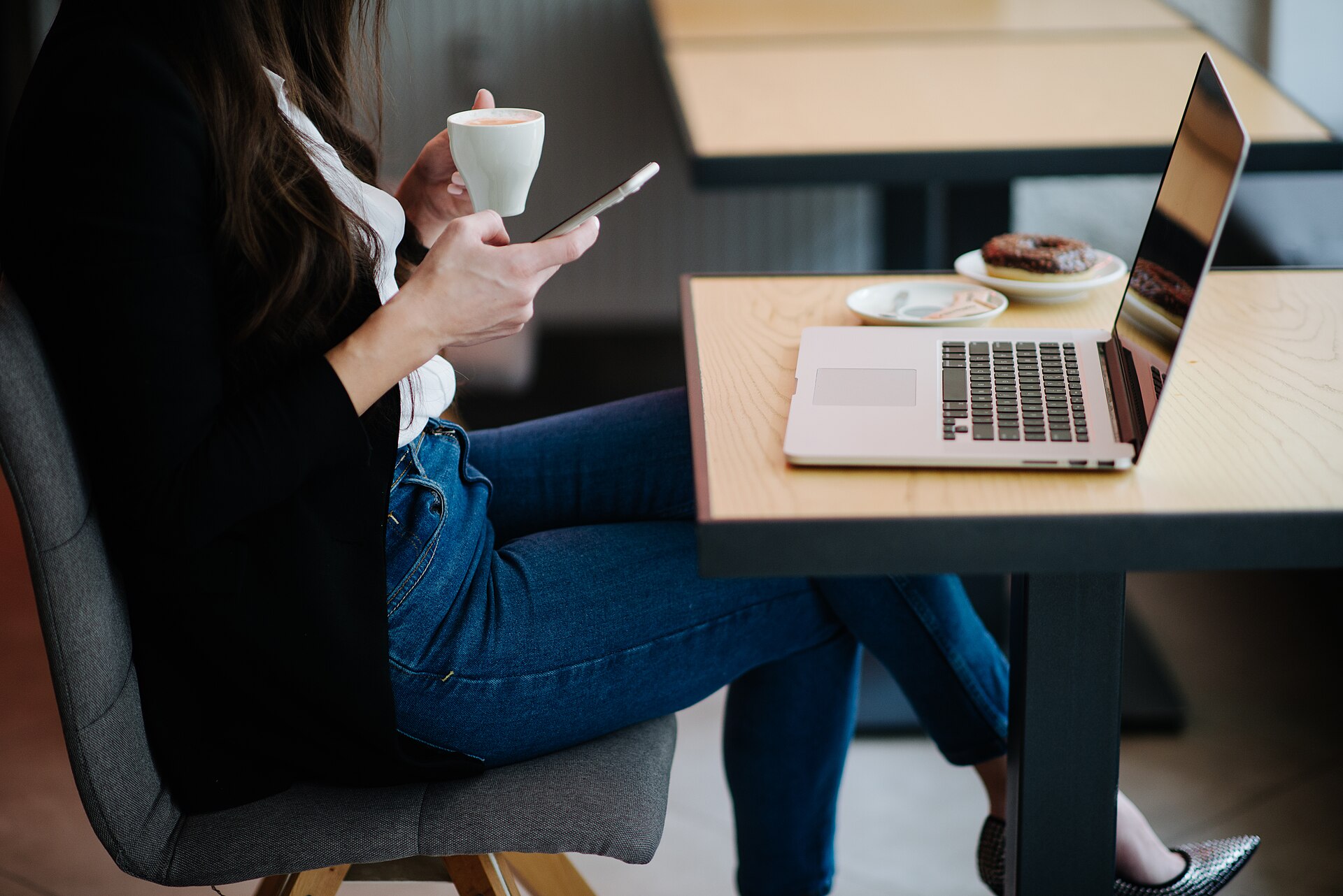 A woman using a smartphone beside a laptop in a cafe