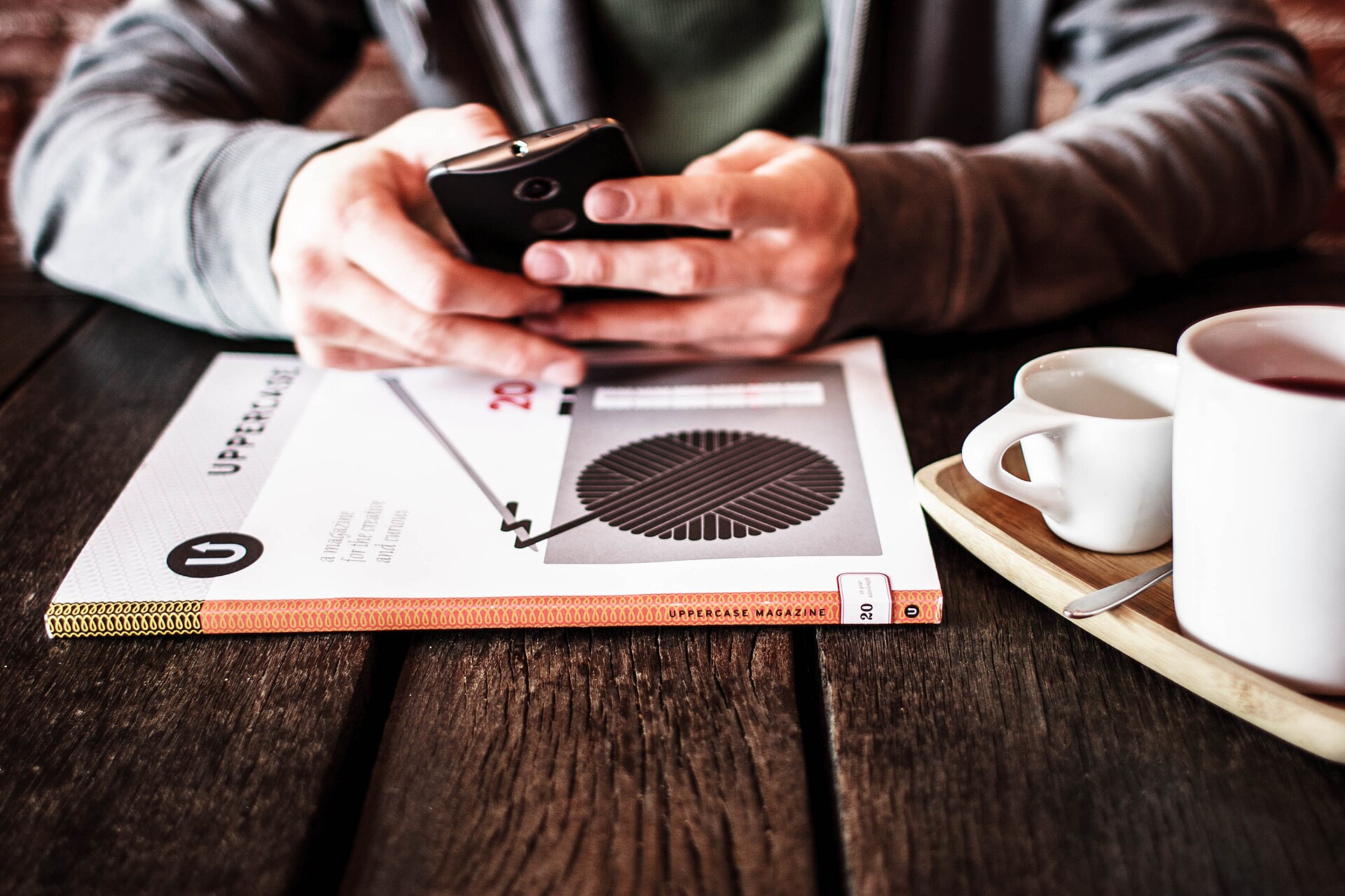 Hands using a smartphone over a notebook in a cafe