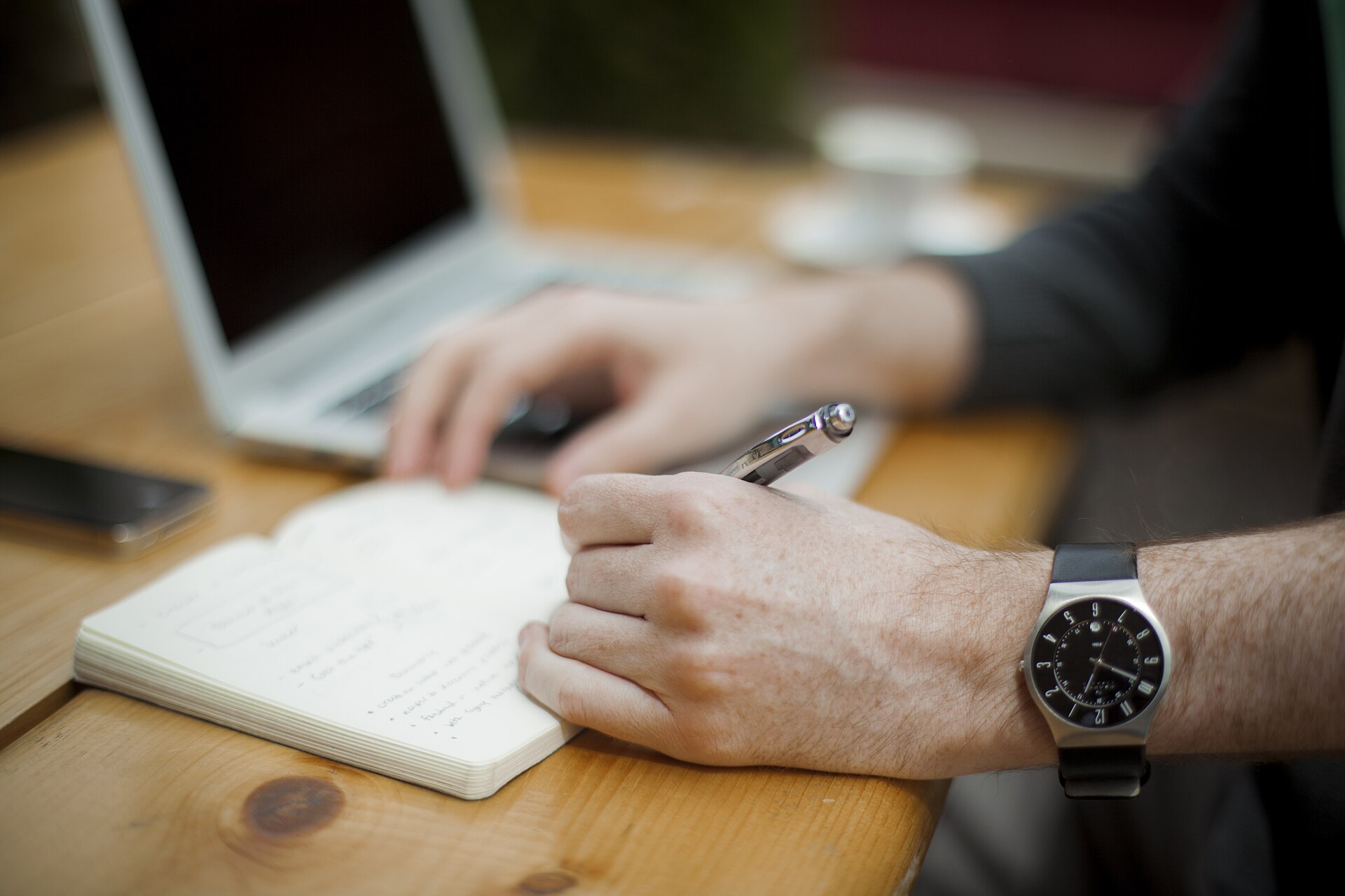 A person writing notes beside a laptop