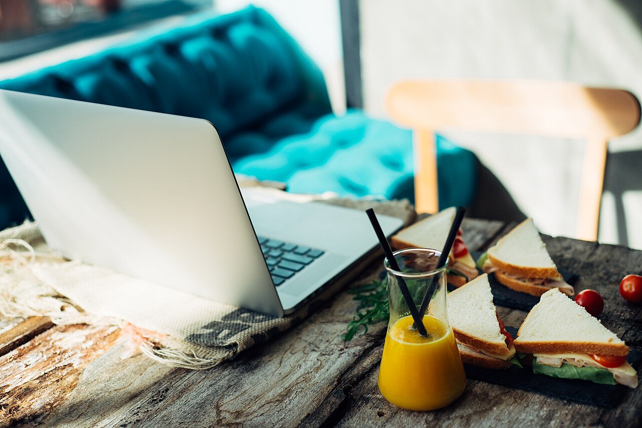 Workspace with laptop, sandwich, and juice during afternoon in a cozy cafe setting