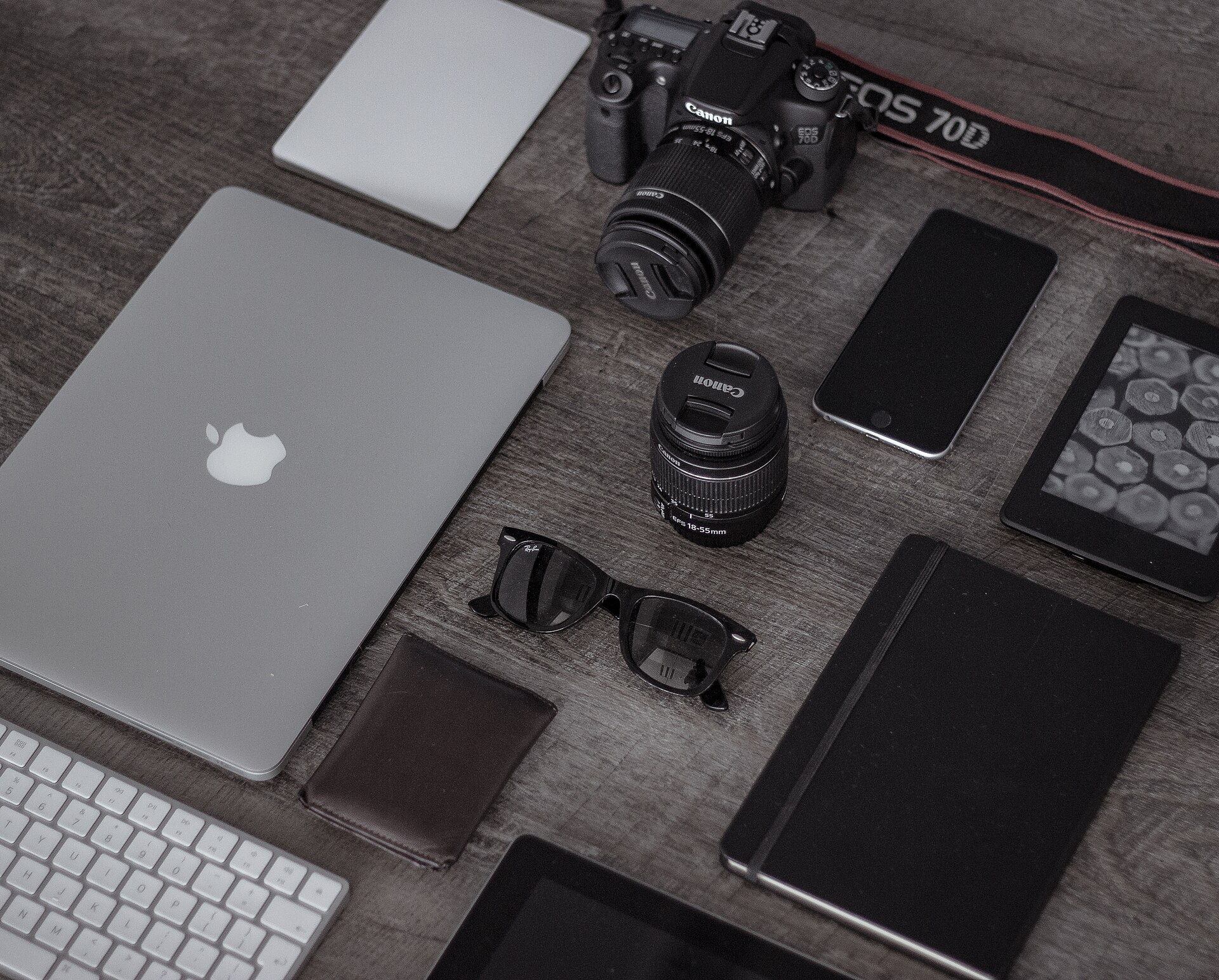 A laptop, phone, notebook and camera on a desk