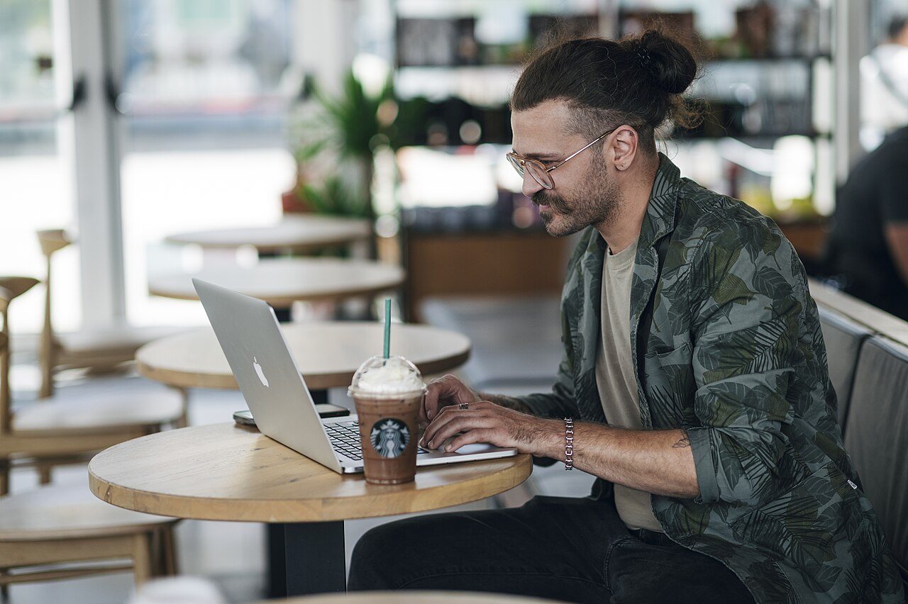 Man working on laptop while enjoying a cold beverage in a cozy cafe setting
