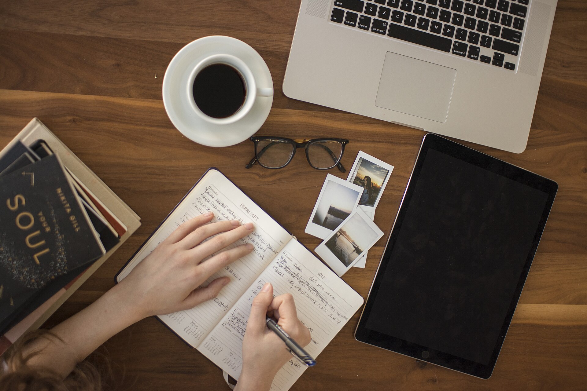 A person journalling beside travel photographs and a laptop